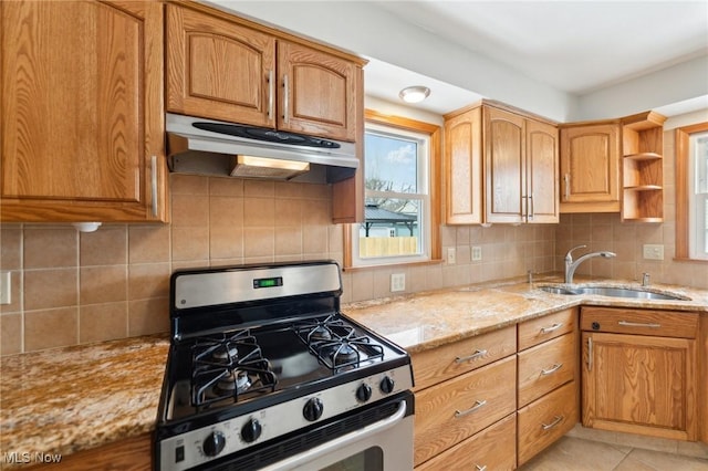 kitchen featuring tasteful backsplash, under cabinet range hood, gas range, light stone counters, and a sink