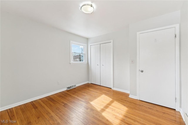 unfurnished bedroom with light wood-style flooring, baseboards, visible vents, and a closet