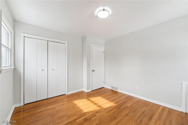 unfurnished bedroom with wood finished floors, visible vents, a closet, and baseboards