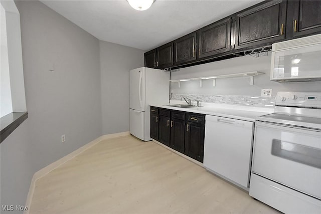 kitchen featuring light wood finished floors, dark cabinets, light countertops, white appliances, and a sink