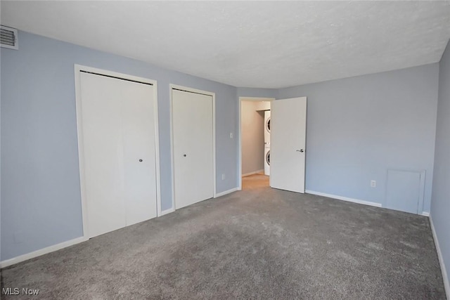 unfurnished bedroom featuring visible vents, two closets, stacked washer and dryer, carpet flooring, and baseboards