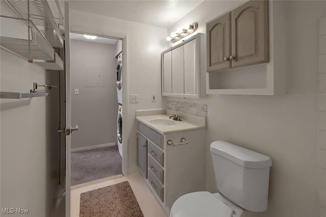 bathroom with stacked washer / dryer, toilet, vanity, and baseboards