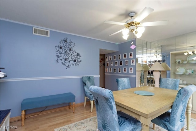 dining space with visible vents, wood finished floors, ceiling fan, and ornamental molding