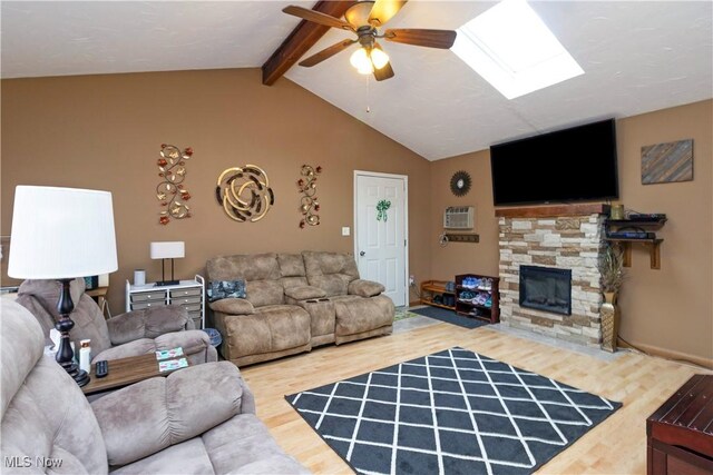 living area featuring lofted ceiling with skylight, a stone fireplace, a ceiling fan, and wood finished floors