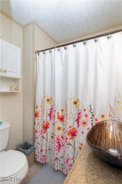 full bathroom featuring curtained shower, toilet, tile walls, and a sink