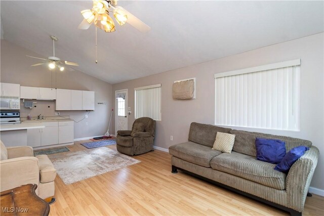 living room featuring lofted ceiling, light wood-style flooring, and baseboards