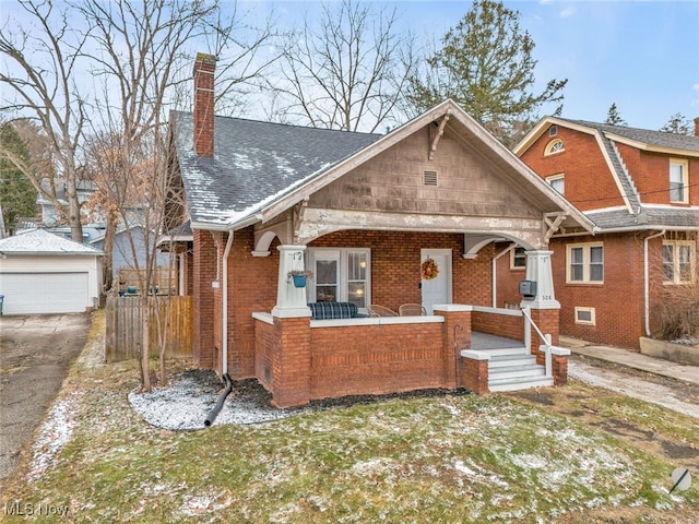 view of front facade featuring an outbuilding, covered porch, a chimney, a shingled roof, and brick siding