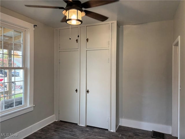 unfurnished bedroom with a ceiling fan, baseboards, visible vents, dark wood-style flooring, and a closet