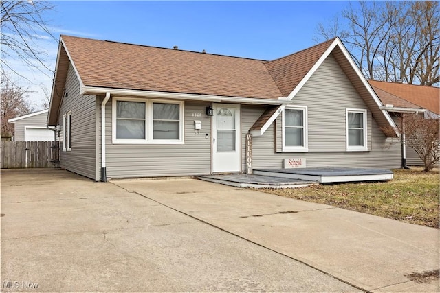 view of front of house with a garage, roof with shingles, and fence