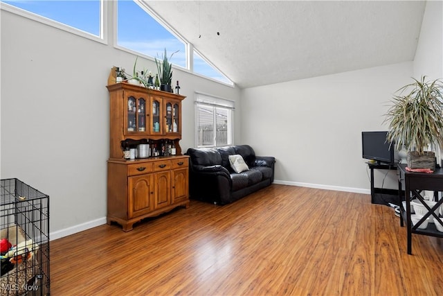 sitting room featuring high vaulted ceiling, light wood-type flooring, and baseboards