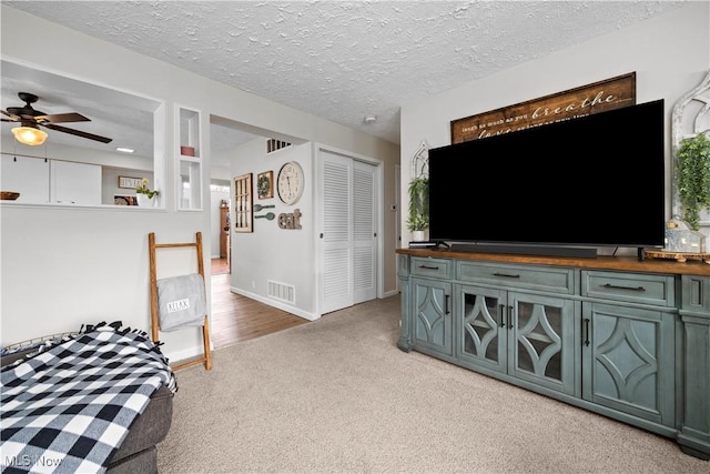 living room featuring a textured ceiling, ceiling fan, visible vents, and light carpet