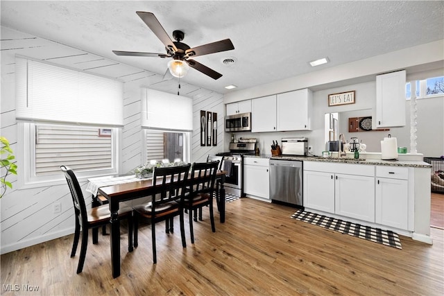 dining space featuring baseboards, visible vents, ceiling fan, light wood-style floors, and a textured ceiling