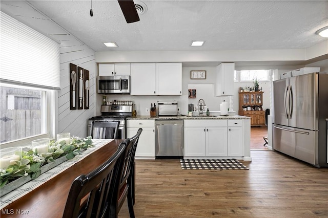 kitchen with white cabinets, appliances with stainless steel finishes, wood finished floors, and a sink