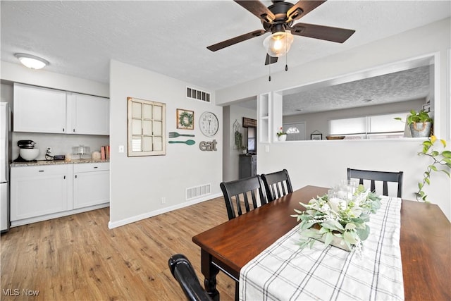 dining space with baseboards, visible vents, light wood finished floors, and a textured ceiling