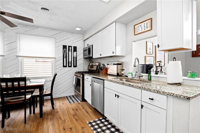 kitchen featuring visible vents, appliances with stainless steel finishes, light wood-style floors, white cabinets, and a sink