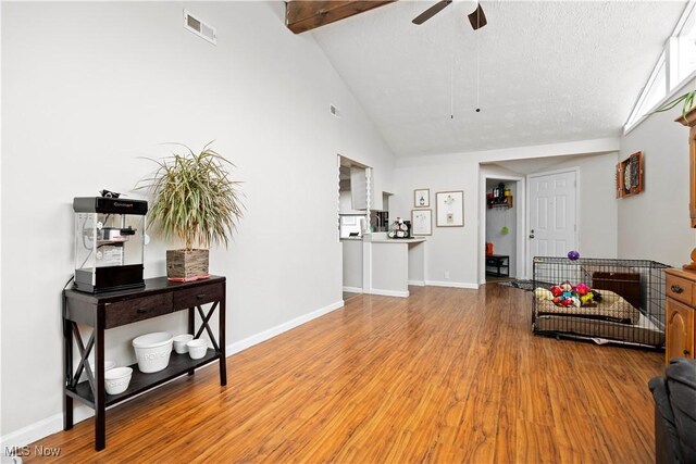 interior space featuring visible vents, a ceiling fan, wood finished floors, baseboards, and vaulted ceiling with beams