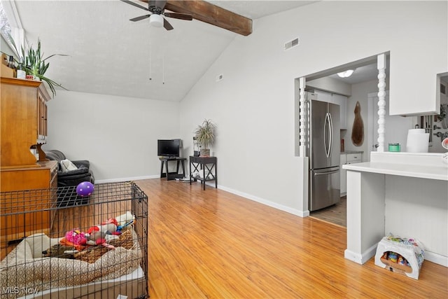 interior space featuring a ceiling fan, visible vents, baseboards, lofted ceiling with beams, and light wood-style floors