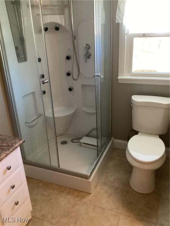 bathroom with toilet, a stall shower, vanity, and baseboards