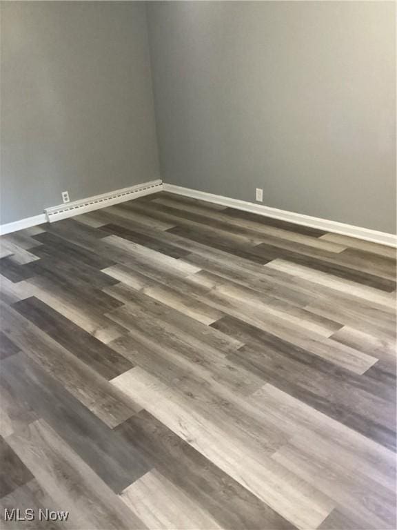 spare room featuring a baseboard heating unit, baseboards, and wood finished floors