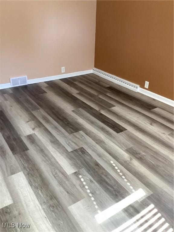 interior details with a baseboard heating unit, wood finished floors, visible vents, and baseboards