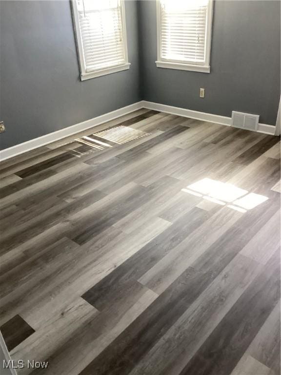 spare room featuring wood finished floors, visible vents, and baseboards