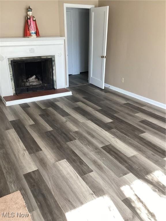 unfurnished living room featuring a fireplace with raised hearth, dark wood-type flooring, and baseboards