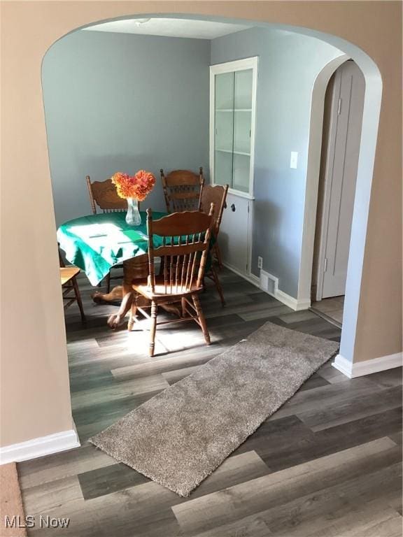 dining area with arched walkways, visible vents, baseboards, and wood finished floors