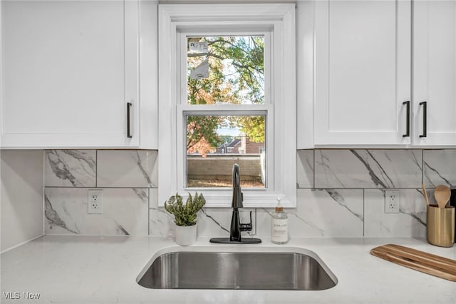 kitchen with tasteful backsplash, white cabinets, light stone countertops, and a sink