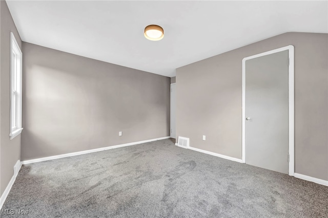 spare room with vaulted ceiling, carpet, visible vents, and baseboards