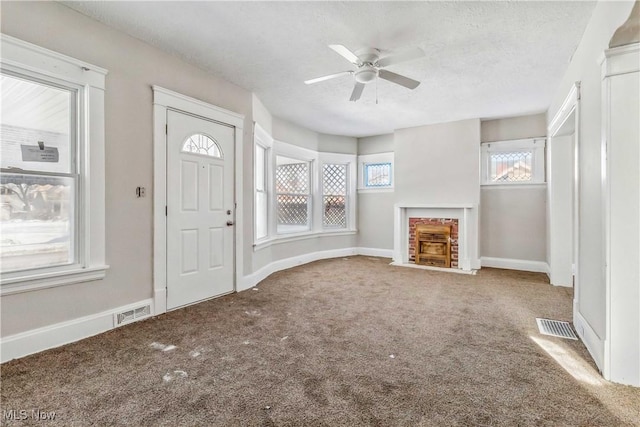 interior space with visible vents, baseboards, ceiling fan, a fireplace with flush hearth, and a textured ceiling