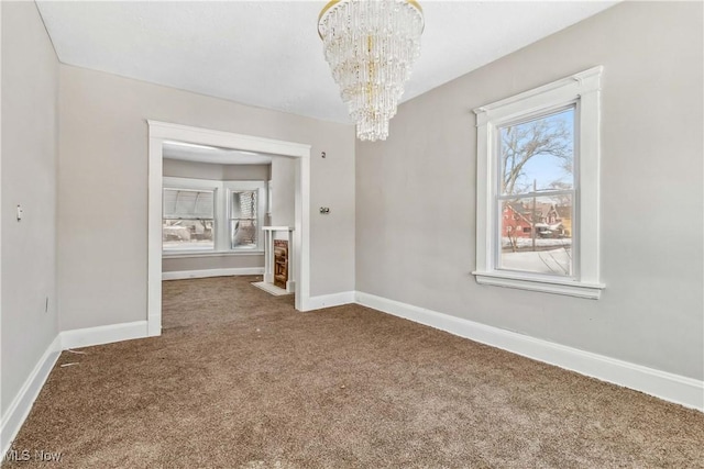 unfurnished dining area featuring baseboards, carpet, an inviting chandelier, and a fireplace with flush hearth