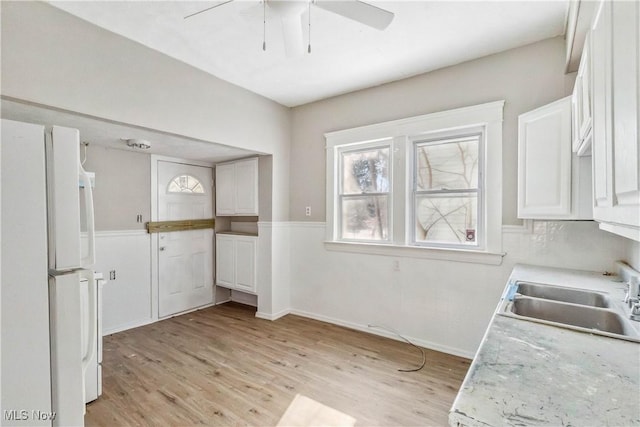 kitchen with light wood-style flooring, freestanding refrigerator, white cabinetry, a ceiling fan, and a sink