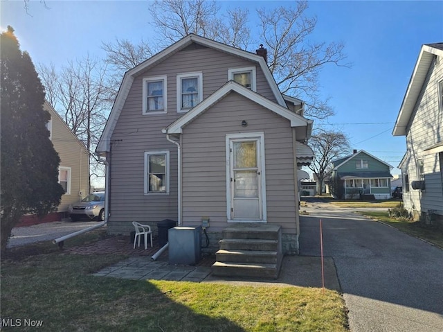 view of front of home featuring a gambrel roof, entry steps, a chimney, and driveway