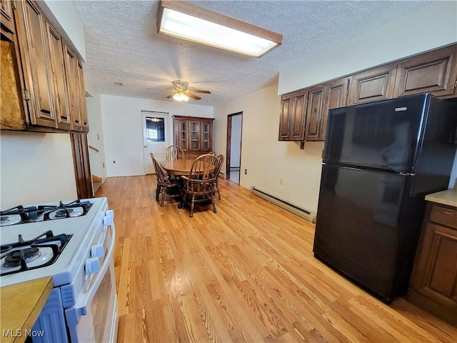 kitchen with light wood-style flooring, a baseboard heating unit, a textured ceiling, freestanding refrigerator, and white gas range