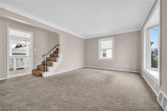 carpeted empty room with stairway, baseboards, visible vents, and an inviting chandelier