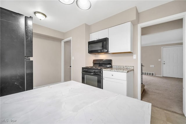 kitchen featuring visible vents, light carpet, black appliances, and white cabinets