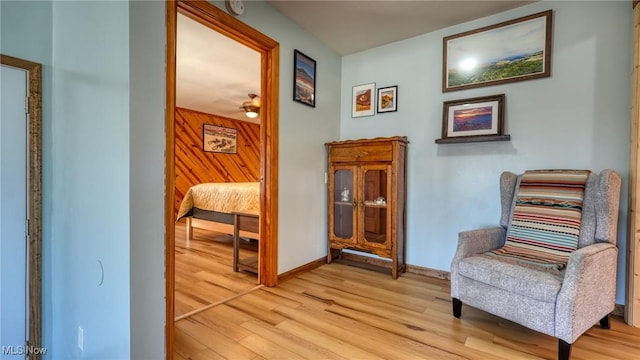 living area with baseboards, light wood-style floors, and wood walls