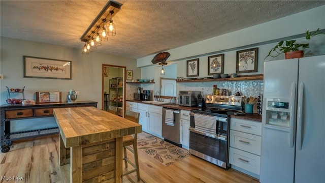 kitchen with light wood finished floors, a textured ceiling, stainless steel appliances, and a sink