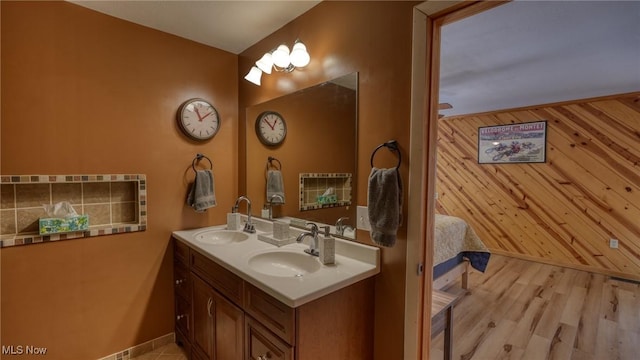 full bathroom with double vanity, wood finished floors, wood walls, and a sink