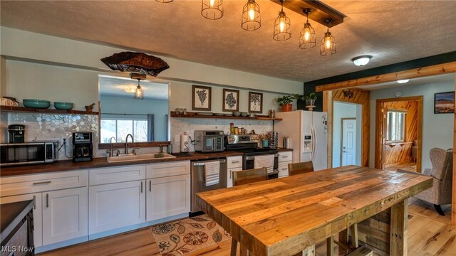 kitchen with butcher block counters, stainless steel appliances, light wood-type flooring, and a sink