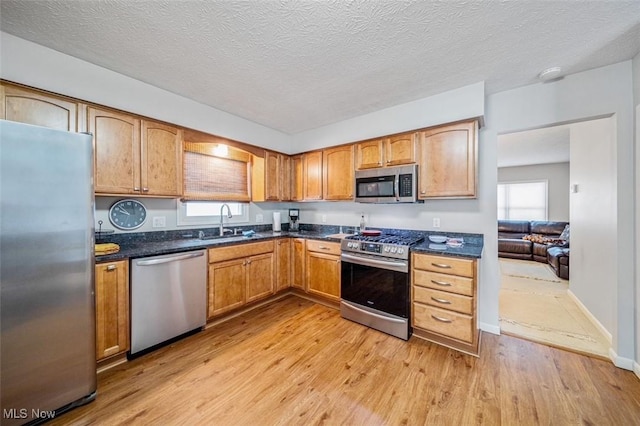 kitchen featuring baseboards, a sink, stainless steel appliances, light wood-style floors, and a textured ceiling