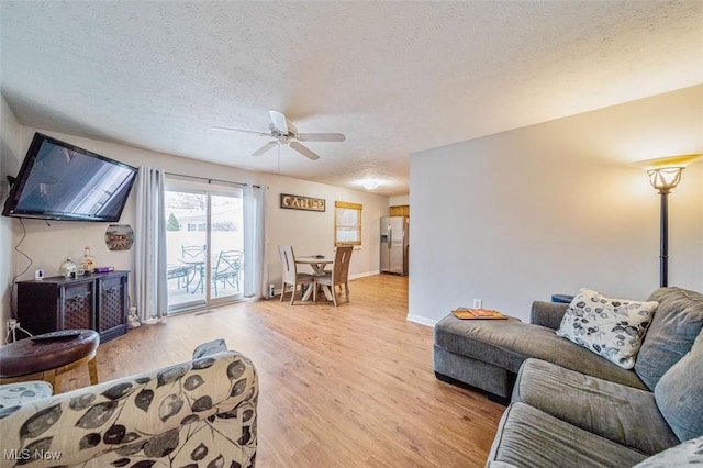 living area with baseboards, a textured ceiling, light wood-type flooring, and a ceiling fan