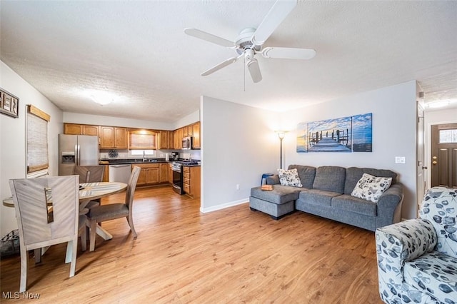 living room featuring baseboards, a textured ceiling, light wood-type flooring, and a ceiling fan