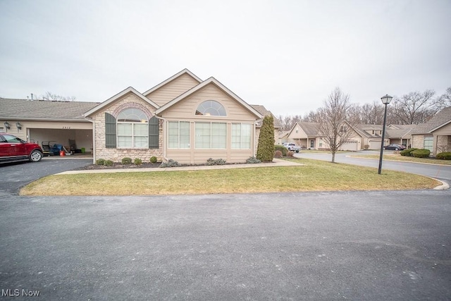 ranch-style home featuring brick siding, an attached garage, a residential view, a front yard, and driveway