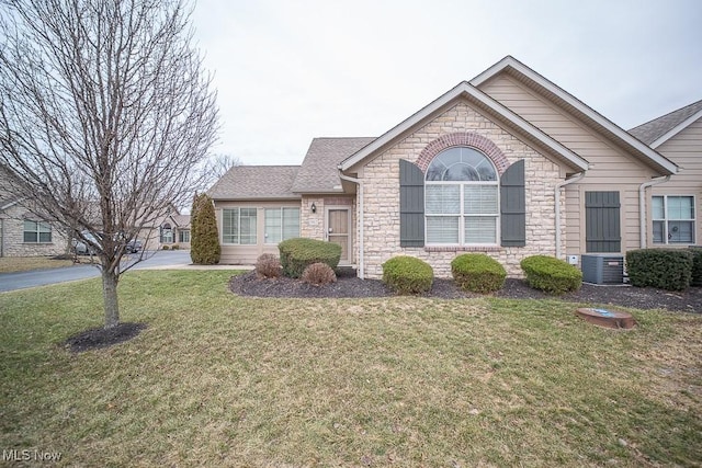 ranch-style home featuring a front yard, cooling unit, stone siding, and roof with shingles