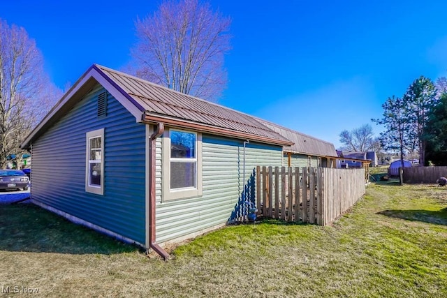 view of property exterior featuring metal roof, a lawn, and fence