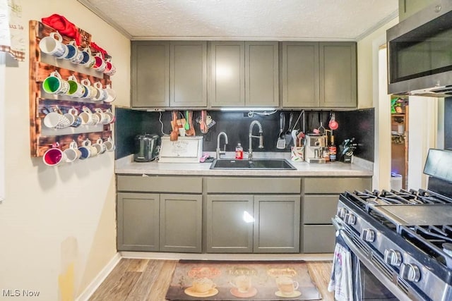 kitchen with a sink, a textured ceiling, appliances with stainless steel finishes, light wood finished floors, and light countertops
