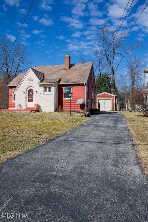 view of front of property with an outbuilding, a chimney, a front lawn, a garage, and aphalt driveway