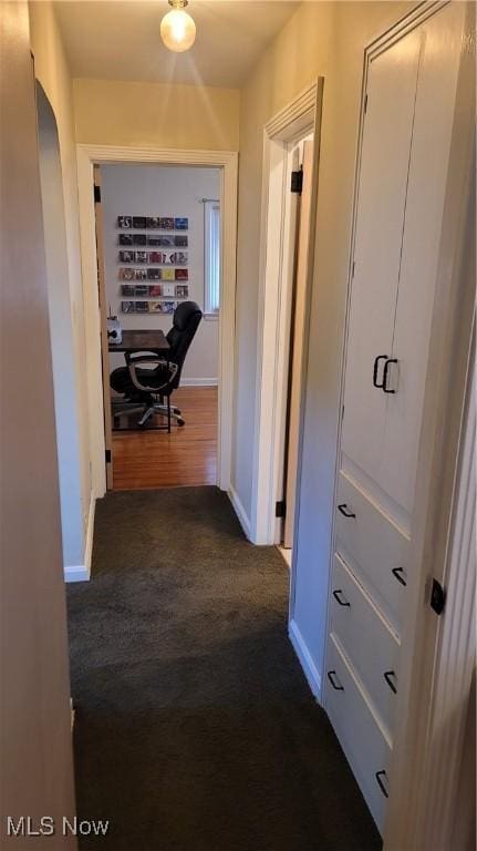 hallway with arched walkways, baseboards, and dark colored carpet