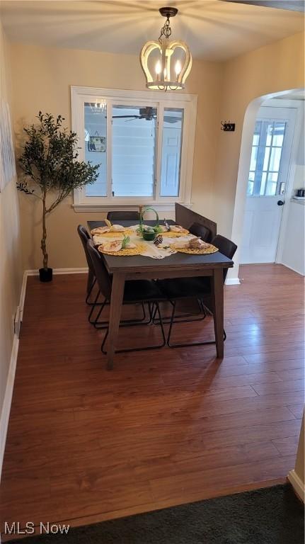 dining area with arched walkways, a chandelier, baseboards, and wood finished floors